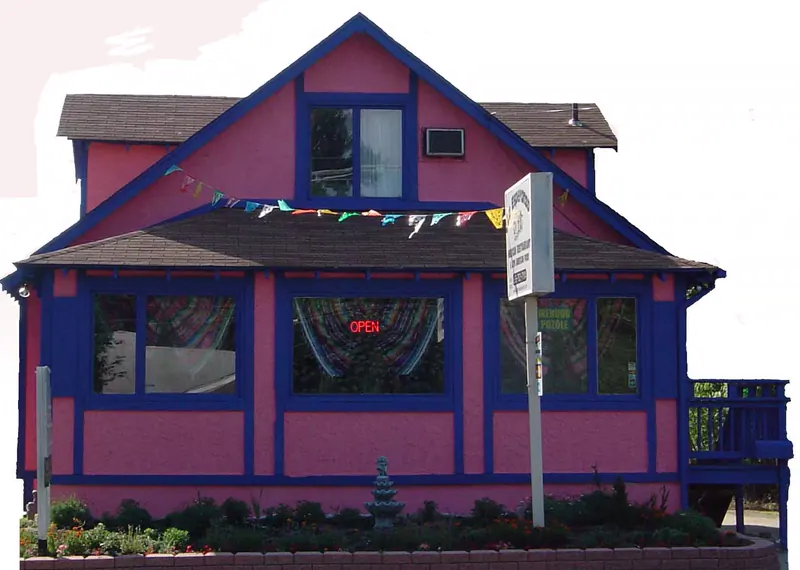 The pink and violet-blue front of the house with the open sign and a string of pennant flags