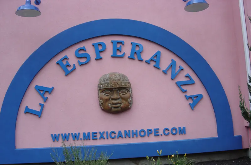 The blue arch sign reading La Esperanza with a carved stone head, on the pink wall of the restaurant