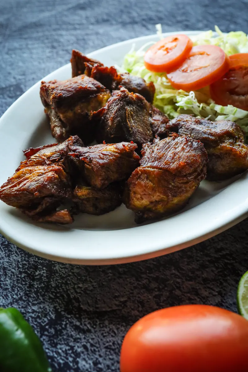 Carnitas de puerco: crisp fried pork chunks with shredded lettuce and tomato on a white oval plate, on dark slate