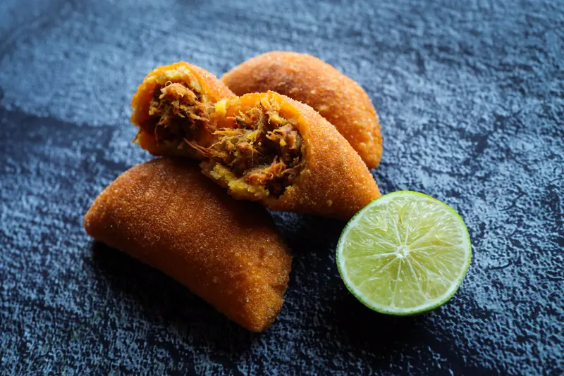 An empanada split open to show its beef and potato filling, beside a halved lime on slate