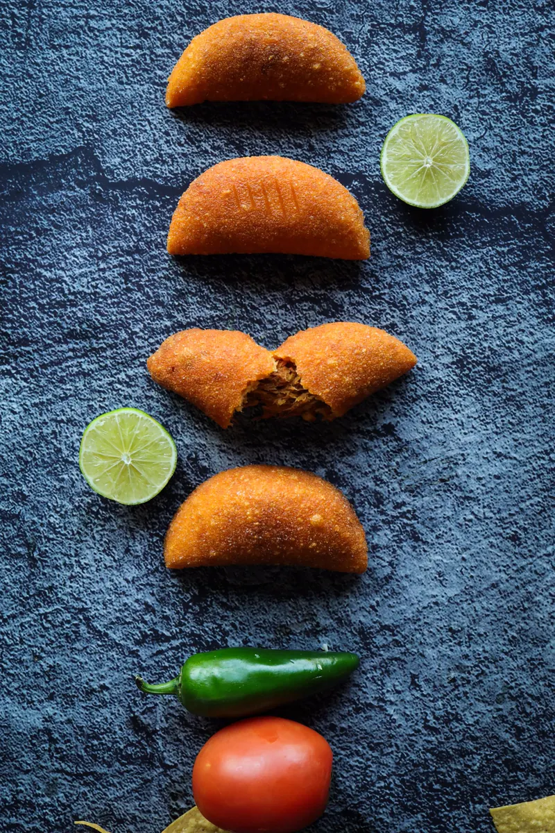 Fried empanadas arranged on slate with a chile and a tomato