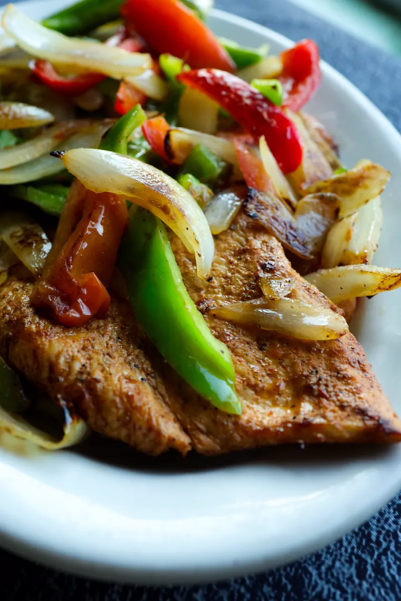 A close-up of sizzling fajitas: grilled chicken with charred peppers and onions on a white plate