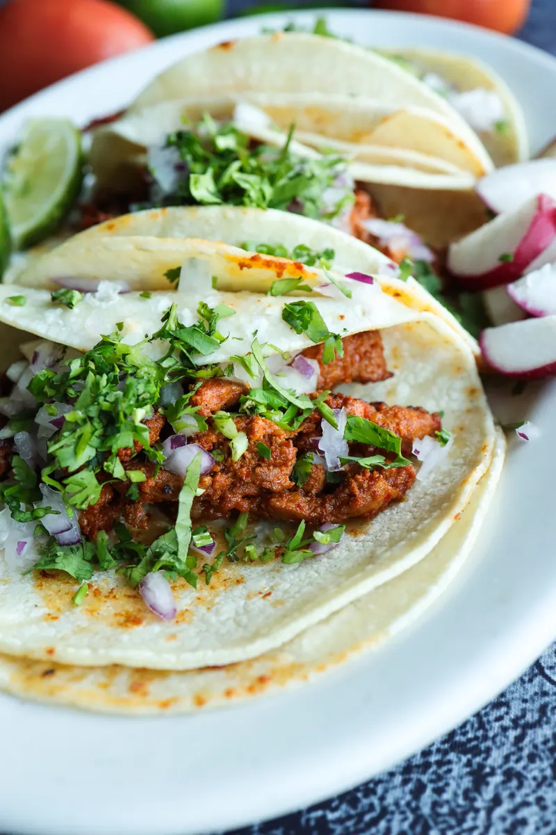 Close-up of three soft tacos with chopped cilantro, onion and radish