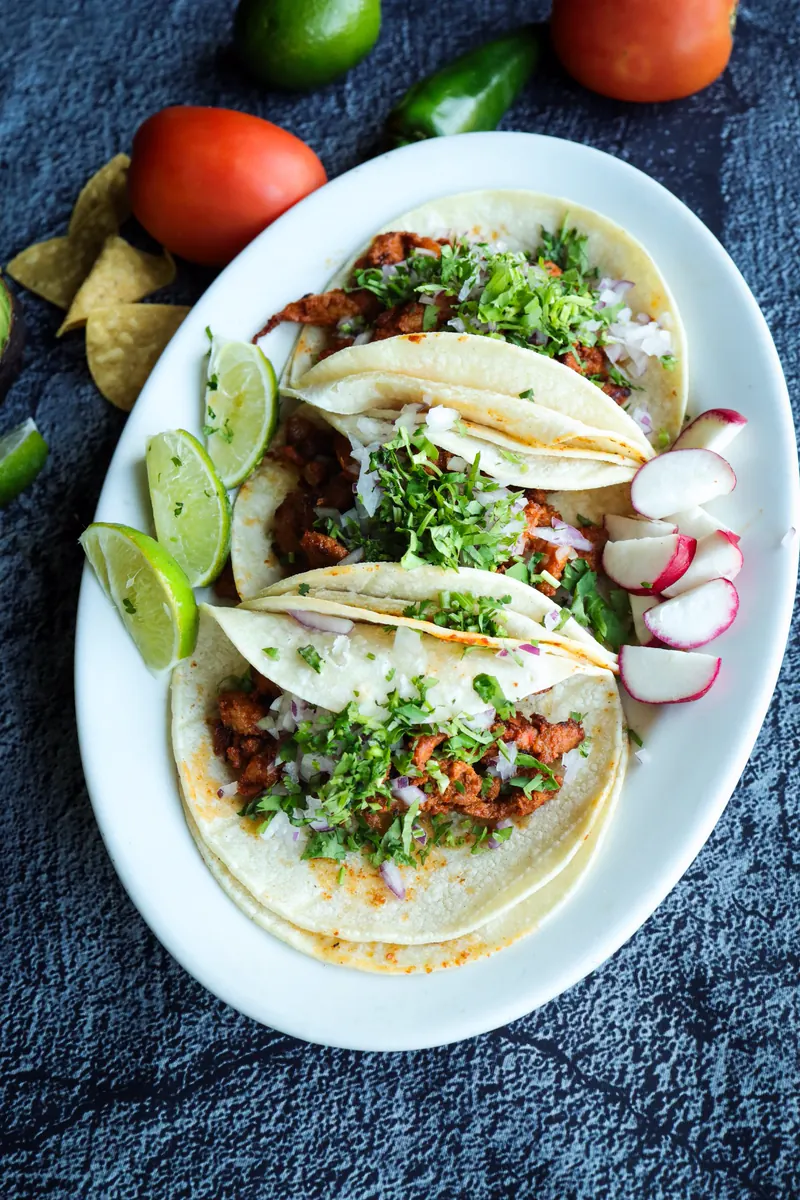 Three soft tacos with cilantro, onion, radish and lime
