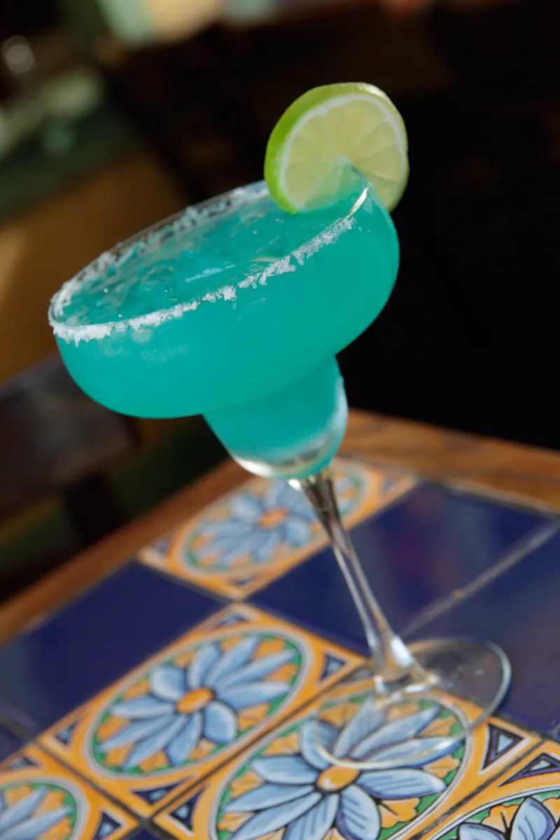 A blue margarita with a salted rim and a lime wheel on blue-and-yellow Talavera tile