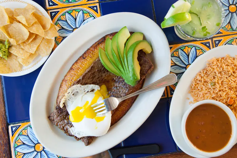Bistec a la criolla on a blue tile table, with rice and a margarita beside it