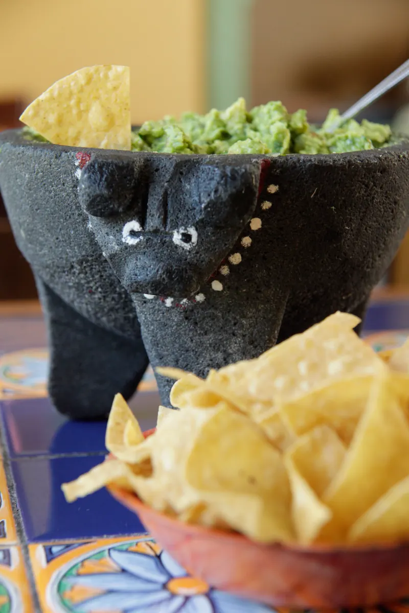 The bull-shaped stone molcajete full of guacamole, chips spilling beside it