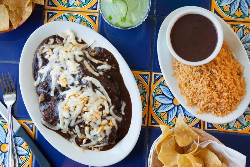 Enchiladas de mole poblano with melted cheese beside rice, black beans and a margarita on blue Talavera tile